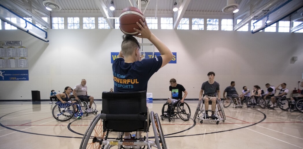 person in wheelchair about to throw a basketball to waiting players.