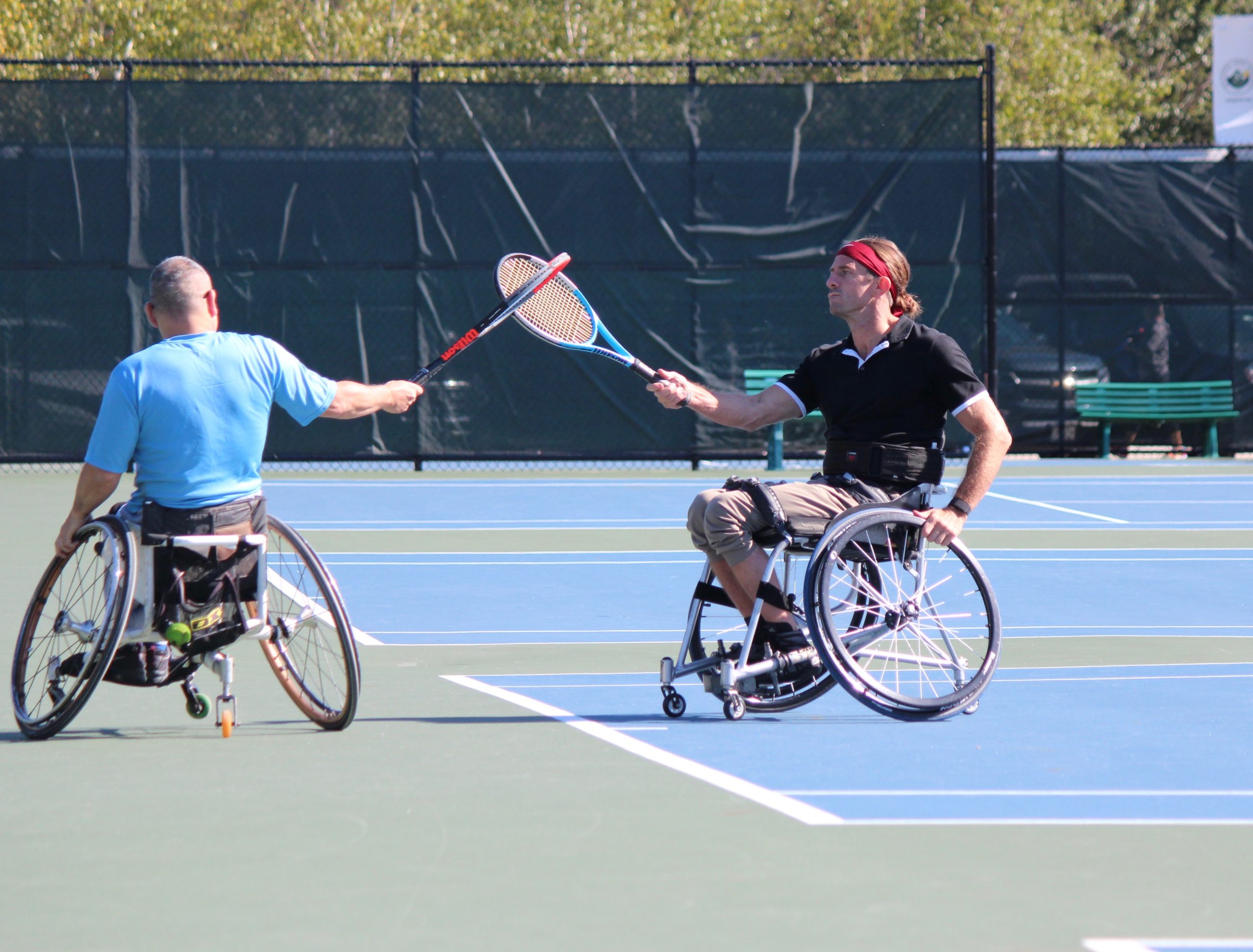 2 wheelchair tennis players celebrating by touching racquets.