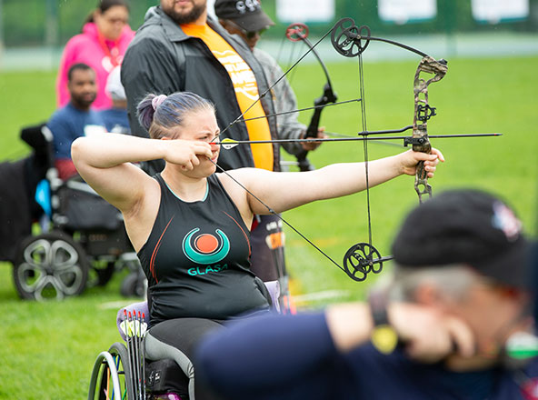 Girl in GLASA Tank top with bow pulled in front of her face surrounding by other archers.