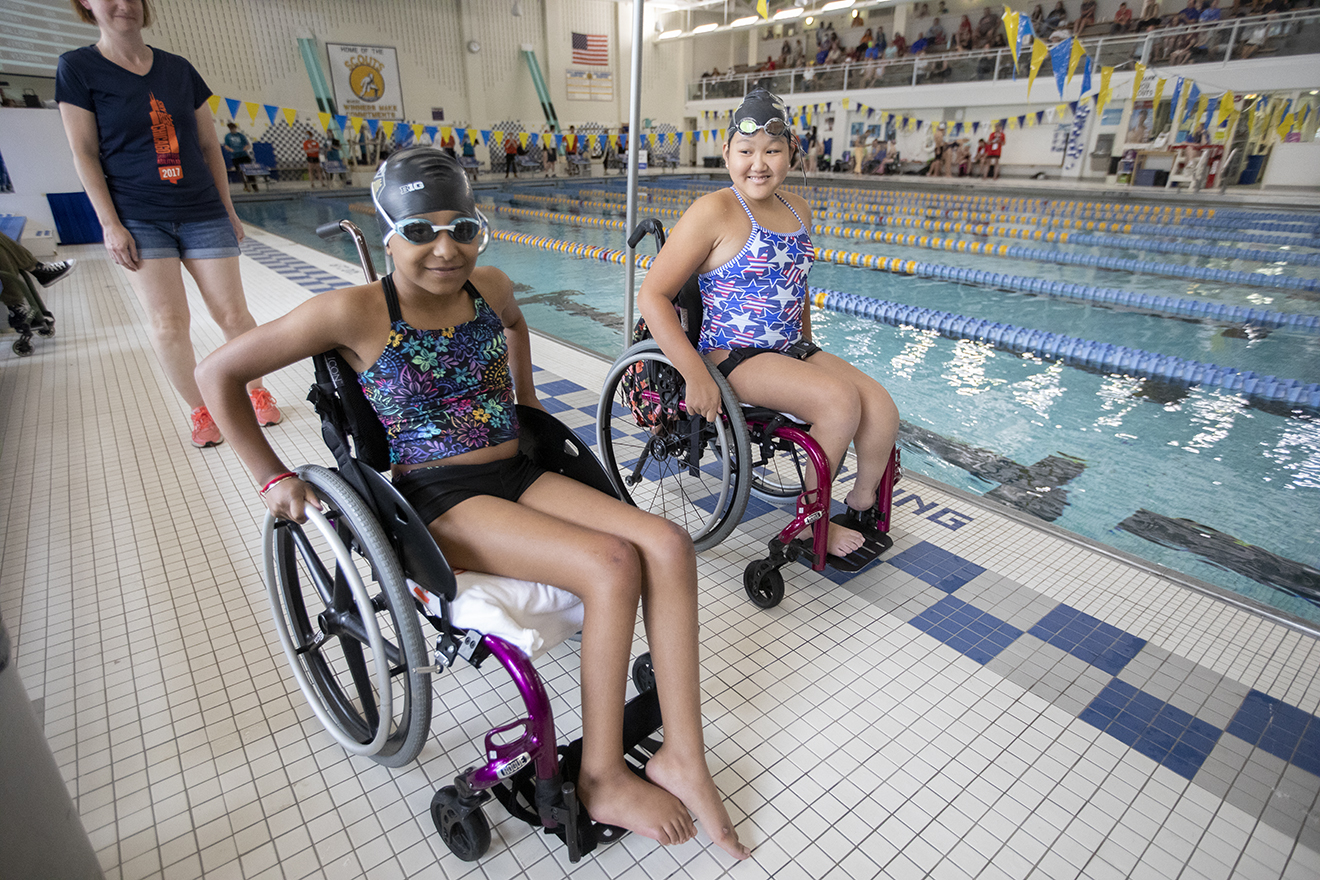 Two girls in wheelchairs by a swimming pool.