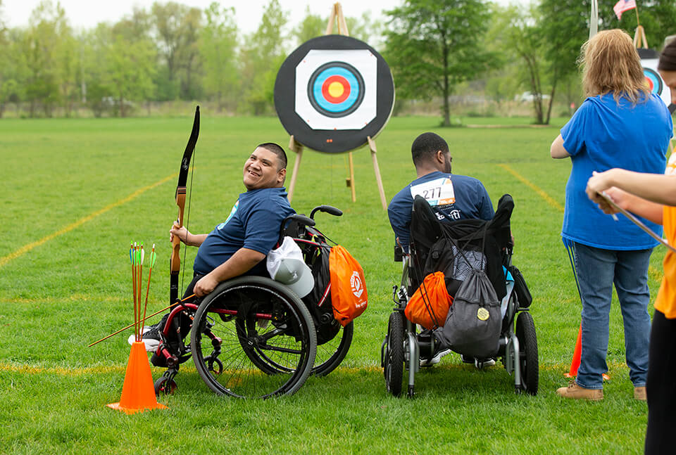 Two people in wheelchairs in front of archery target.